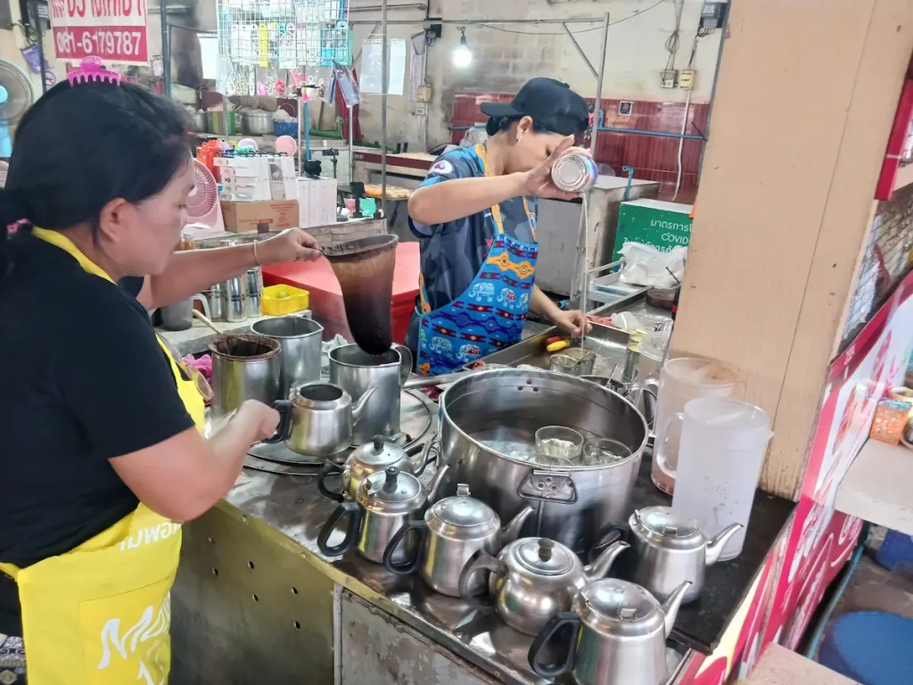 市場の食堂でチャイを作る二人の女性スタッフ。高い位置からチャイを注ぐ人と、お茶をこす人