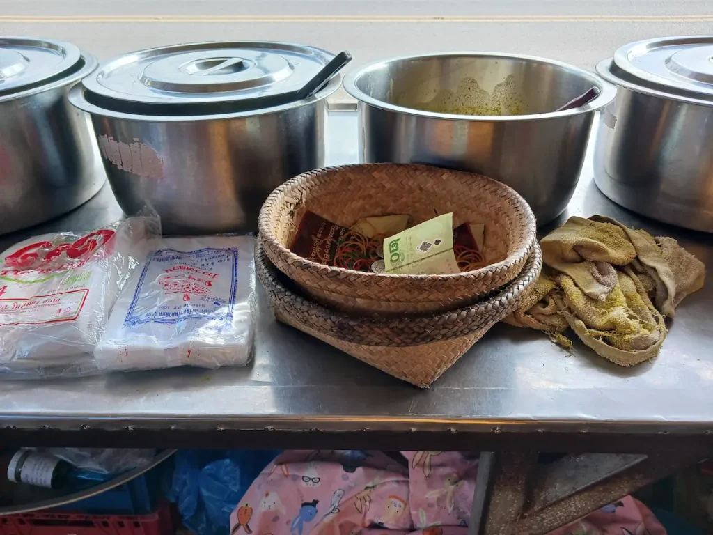 釣り銭が入れてある使い込まれ飴色に変化したカチュー(水草の一種)のトレイ。傍らには屋台のお鍋が並ぶ