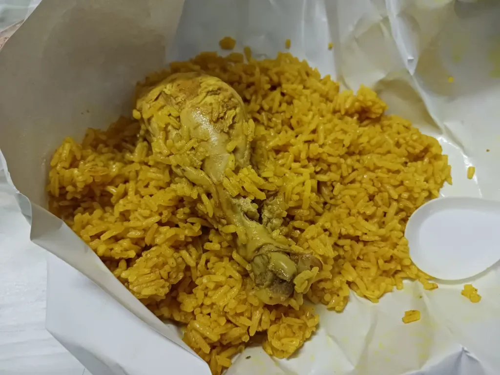 白い包装紙に包まれたスパイスで黄色くなったお米と鶏の手羽先。