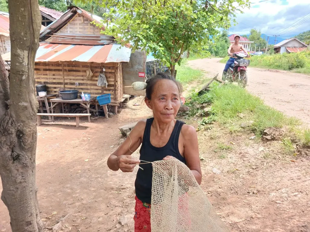 ラオス北部カム族が住む村でタンクトップに巻きスカート姿の老婆が葛バッグを編んでいる