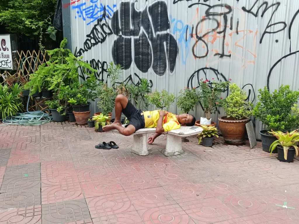 半袖短パン姿の男性が屋外のベンチで体をはみ出しながら寝ている