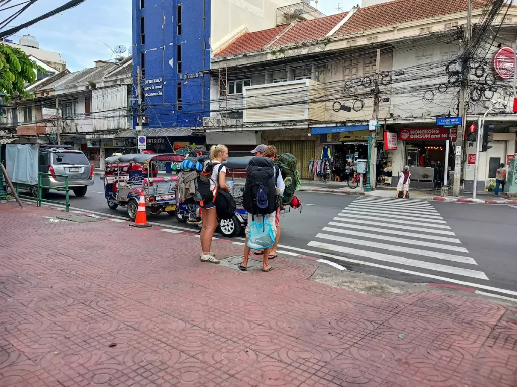 半袖短パンにビーチサンダル姿の男女三人が、大きなリュックを背負って信号待ちをしている