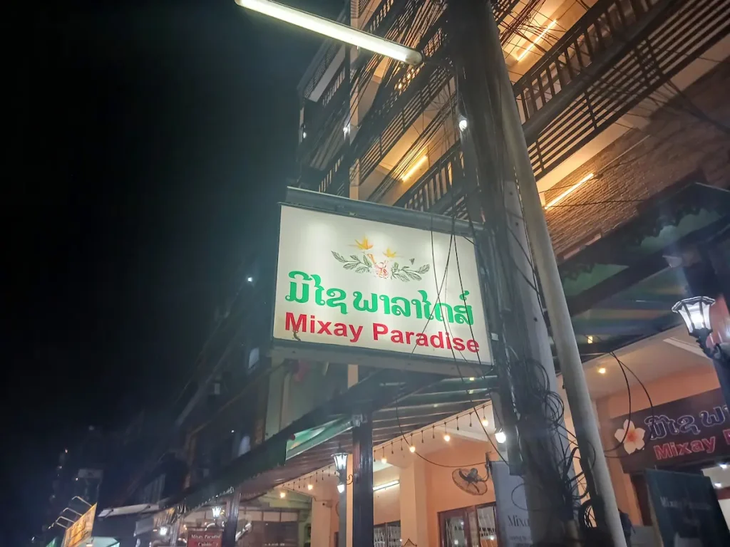 柱から垂れ下がるMixayParadiseHotel と書かれた夜のビエンチャンの街中で光る看板。