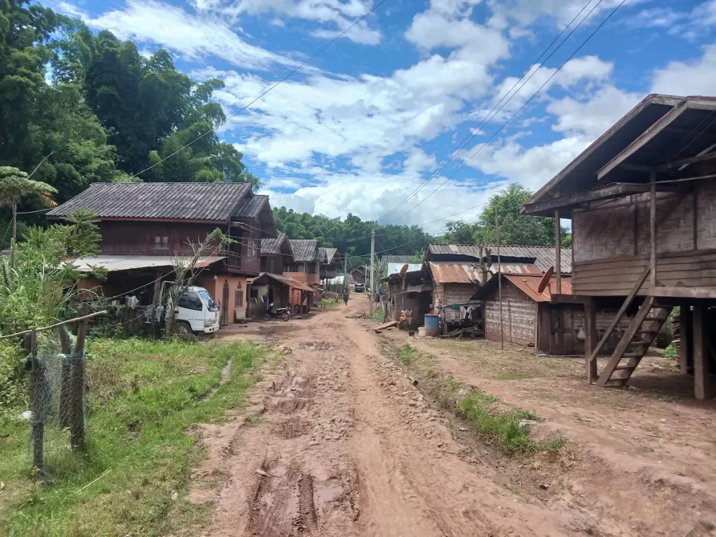ラオス北部カム族の村。舗装されていない土の道路脇に並ぶ木造トタン屋根の家々